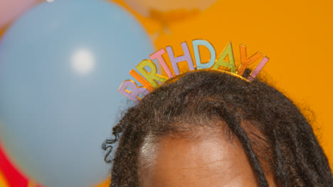 Close-Up-Studio-Portrait-Of-Woman-Wearing-Birthday-Headband-Celebrating-With-Balloons